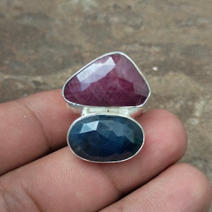 May include: A silver ring featuring a large, faceted, dark blue gemstone and a smaller, faceted, pink gemstone.