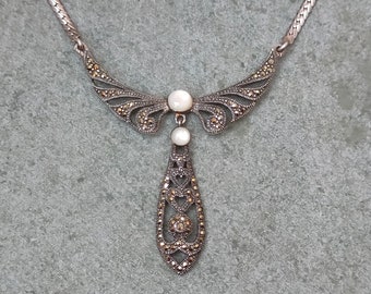 Peut inclure: Un collier en argent avec un pendentif en forme de larme orné de pierres de marcassite. Le pendentif est attaché à une délicate chaîne en argent avec un motif d'aile incrusté de marcassite.