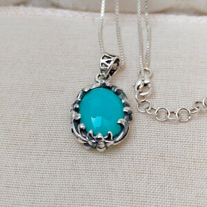 May include: A silver chain necklace with a turquoise oval pendant. The pendant has a detailed silver design around the stone.