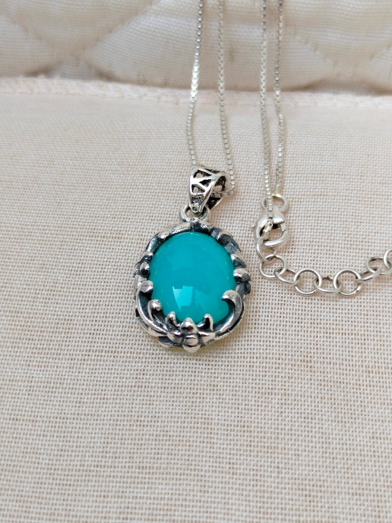 May include: A silver chain necklace with a turquoise oval pendant. The pendant has a detailed silver design around the stone.