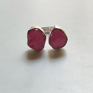 Peut inclure: Une bague en argent avec deux pierres pr&eacute;cieuses roses. Les pierres pr&eacute;cieuses sont de forme irr&eacute;guli&egrave;re et ont un aspect brut et naturel.