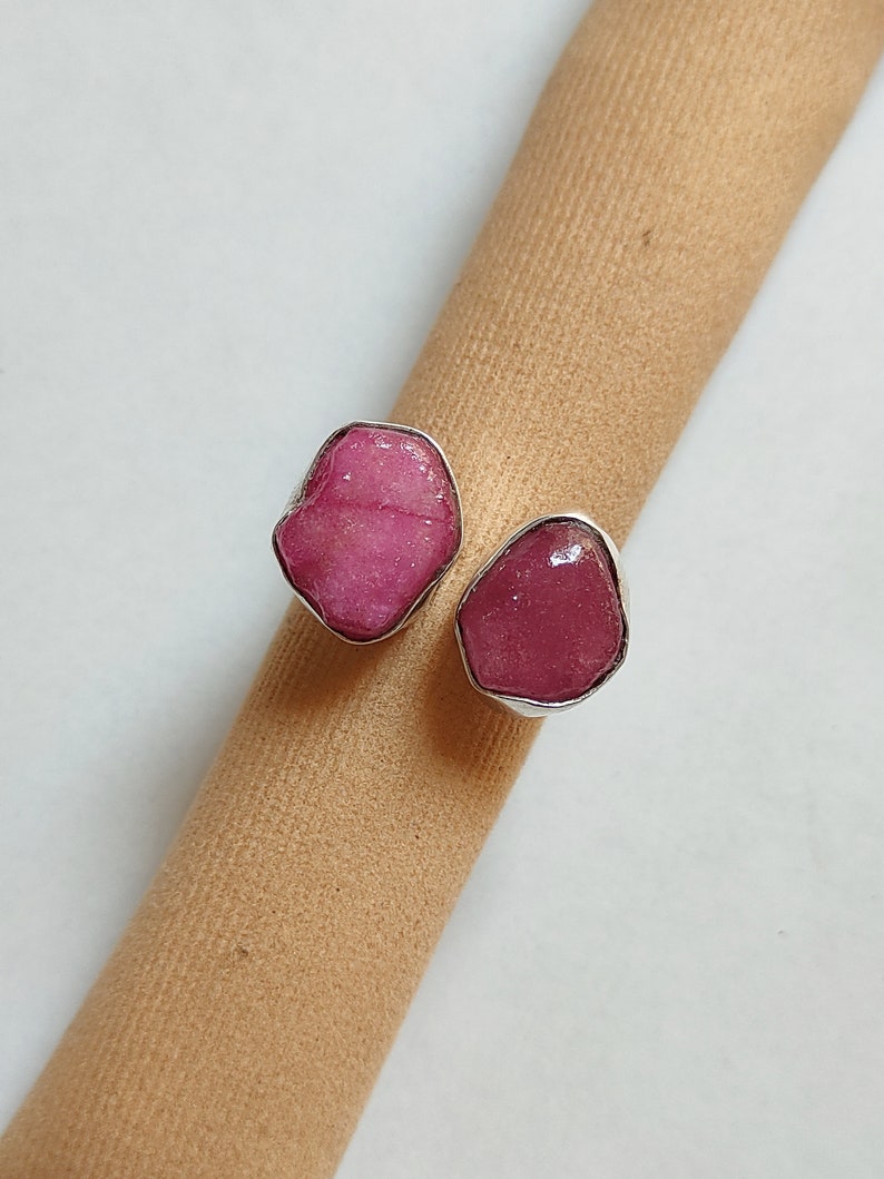 Peut inclure: Deux bagues en argent serties de pierres pr&eacute;cieuses roses. Les bagues sont sur une surface en tissu brun.