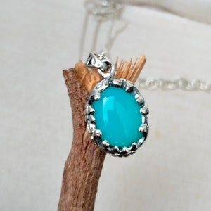 May include: A silver pendant with a turquoise oval gemstone set in a detailed silver frame. The pendant is hanging from a silver chain.