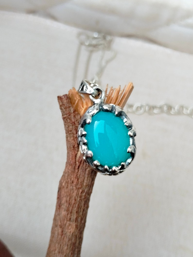May include: A silver pendant with a turquoise oval gemstone set in a detailed silver frame. The pendant is hanging from a silver chain.