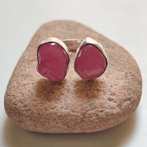 Peut inclure: Une bague en argent avec deux pierres pr&eacute;cieuses roses. La bague est pos&eacute;e sur une roche brune.