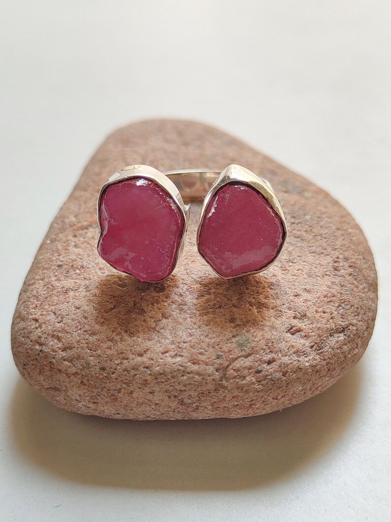 Peut inclure: Une bague en argent avec deux pierres pr&eacute;cieuses roses. La bague est pos&eacute;e sur une roche brune.