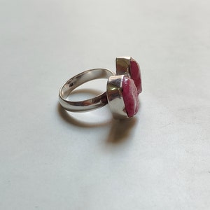 Peut inclure: Une bague en argent avec deux pierres pr&eacute;cieuses roses. La bague est pos&eacute;e sur un fond blanc.