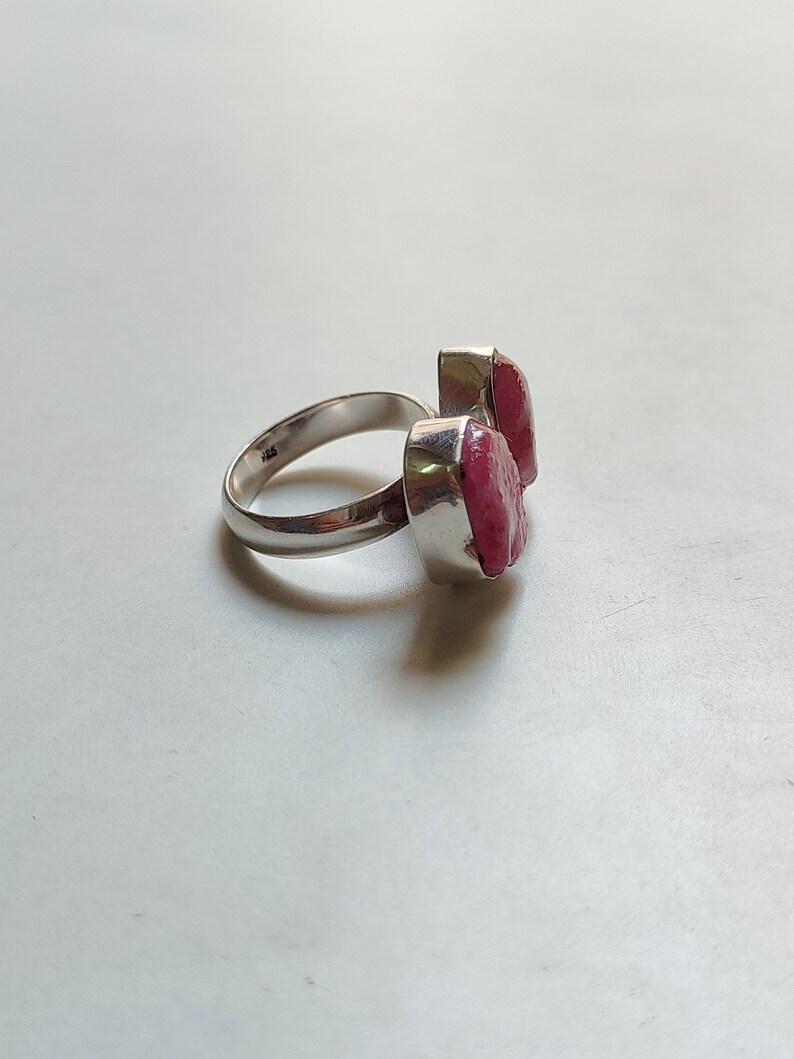 Peut inclure: Une bague en argent avec deux pierres pr&eacute;cieuses roses. La bague est pos&eacute;e sur un fond blanc.