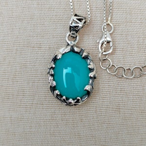 May include: A silver chain necklace with a turquoise oval pendant set in a silver filigree frame.