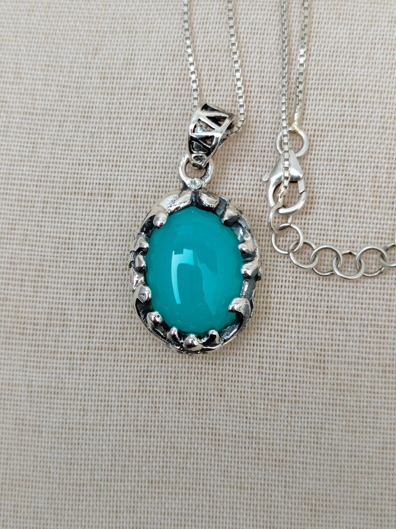 May include: A silver chain necklace with a turquoise oval pendant set in a silver filigree frame.