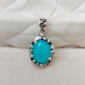 May include: A silver chain necklace with a turquoise oval pendant set in a silver filigree frame.