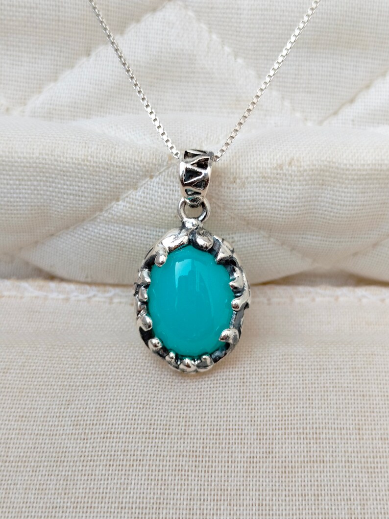 May include: A silver chain necklace with a turquoise oval pendant set in a silver filigree frame.