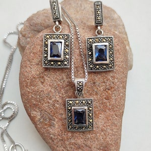 Peut inclure: Un collier et des boucles d'oreilles en argent avec une pierre pr&eacute;cieuse bleue et des accents de marcassite. Le pendentif et les boucles d'oreilles sont de forme carr&eacute;e.