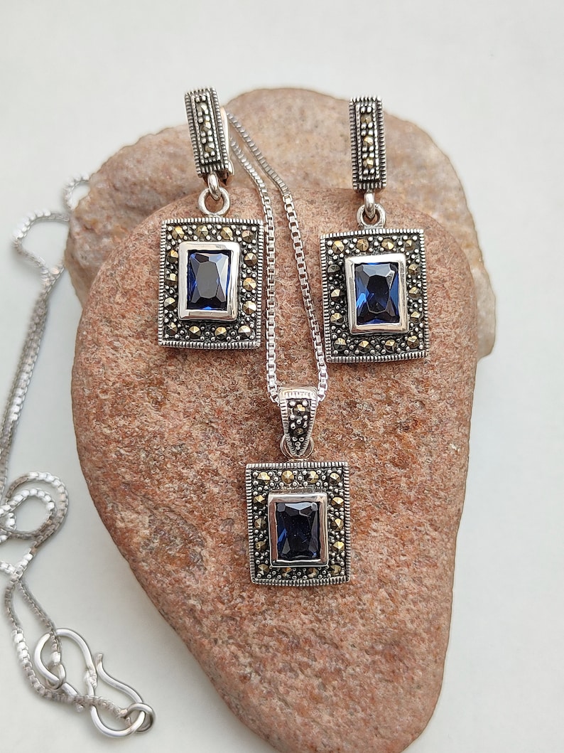 Peut inclure: Un collier et des boucles d'oreilles en argent avec une pierre pr&eacute;cieuse bleue et des accents de marcassite. Le pendentif et les boucles d'oreilles sont de forme carr&eacute;e.