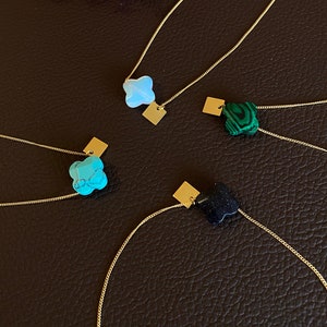 Peut inclure: Quatre colliers en or avec des pendentifs trèfles en pierres précieuses de différentes couleurs. Les pendentifs sont turquoise, vert, noir et blanc.