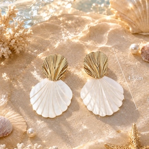 May include: A pair of earrings featuring a gold-toned metal top shell-shaped piece attached to a larger, white, iridescent shell-shaped pendant. The earrings measure 4.5 cm in length. The design showcases a textured metallic finish and a smooth, pearlescent surface on the lower shell component.