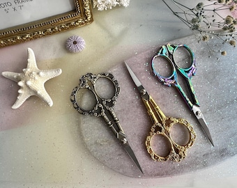 May include: Three pairs of decorative scissors with ornate metal handles. The scissors are silver, gold, and iridescent.