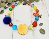 extravagante, kunterbunte Kette mit Resinelementen, Holzfischen, Polarissperlen und Puschel