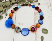 extravagante Kette mit Puschel, Püppchen, Muranoglas und Polarissperlen in kräftigen Farben