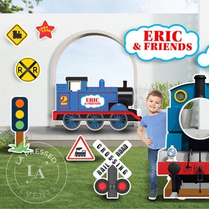 May include: A set of train-themed party decorations featuring a blue locomotive cutout with the text ERIC & FRIENDS, a large blue train front cutout with a face hole, cloud-shaped signs reading ERIC & FRIENDS and HAPPY BIRTHDAY, and various railroad signs.