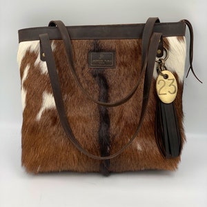 ÚNICO EN SU CLASE ** Colección Jackson Place — Bolso grande de cuero con pelo en piel — Bolso de mano de piel marrón, negro y blanco Bolso de mano con borla de etiqueta de vaca de latón