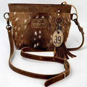 Puede incluir: Bolso bandolera marr&oacute;n y blanco con estampado de lunares y correa de cuero. El bolso tiene forma rectangular con la parte superior de cuero marr&oacute;n y una peque&ntilde;a etiqueta con el n&uacute;mero 39. Tiene una borla y una peque&ntilde;a etiqueta de cuero con la letra "P".