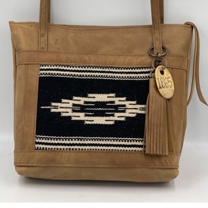 Colección Taos: bolso grande de mano de piel de vaca marrón tostado con tejido en blanco y negro. Colección Jackson Place: bolso de mano tejido a mano