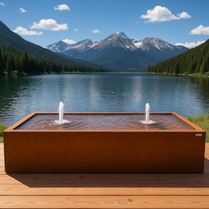 May include: A rectangular outdoor water fountain with two water jets. The fountain is made of a weathered, reddish-brown material and sits on a wooden deck. The background features a lake, mountains, and a blue sky.
