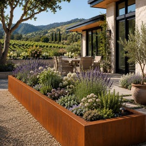 Pode incluir: Uma floreira retangular longa feita de aço corten desgastado na cor ferrugem. A floreira está preenchida com uma variedade de folhagens verdes, espigas de lavanda roxas e pequenas flores brancas, posicionada num caminho de cascalho perto de um pátio.