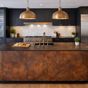 Może przedstawiać: Nowoczesna kuchnia z ciemnymi szafkami, wyspą w odcieniu miedzi i mosiężnymi lampami wiszącymi. Wyspa ma ciemny blat i zaokrąglony kształt. Lodówka ze stali nierdzewnej i marmurowa ściana dodają nowoczesnego charakteru.