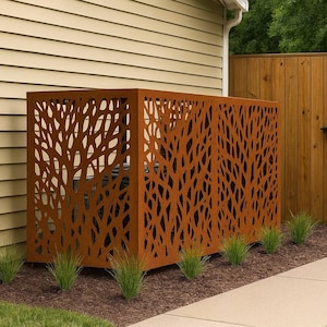 May include: A decorative metal screen with a tree branch design, in a warm brown color, conceals an outdoor unit. The screen is placed near a beige house and a wooden fence, with green grass and plants in the foreground.