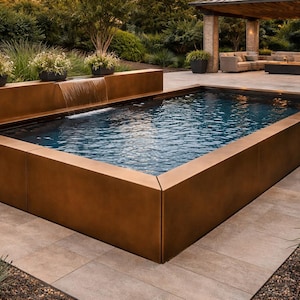 Puede incluir: Una piscina rectangular al aire libre con un interior azul oscuro y un exterior de color bronce. La piscina tiene una pequeña cascada y está rodeada de un patio y paisajismo. La piscina mide aproximadamente 4,6 metros de largo y 2,4 metros de ancho.
