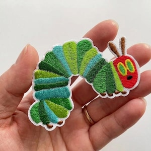 May include: Embroidered patch featuring a colorful caterpillar design. The caterpillar has a red head with yellow eyes and a black mouth. Its body is a mix of green and blue segments, outlined in white.