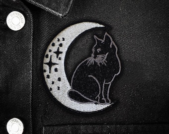 May include: Black cat patch embroidered on a black denim jacket. The patch features a black cat sitting inside a crescent moon with stars. The moon is light gray with small dots.
