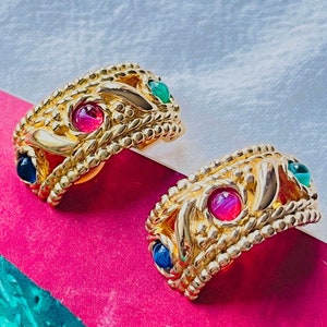May include: A pair of gold-toned earrings with a beaded design and colorful stones. The earrings feature a mix of red, green, and blue stones.