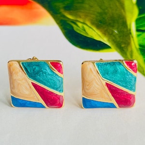 May include: A pair of gold square earrings with a geometric design. The earrings are decorated with blue, teal, pink, and cream enamel.