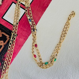 May include: A gold chain necklace with a double strand design. The necklace features small, oval-shaped gemstones in red, blue, and green.