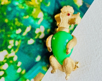 May include: Gold-tone poodle brooch with a green heart-shaped stone and a red rhinestone accent.