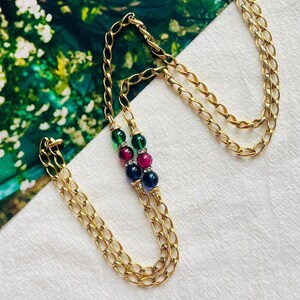 May include: A gold chain necklace with three beads. The beads are green, pink, and blue.