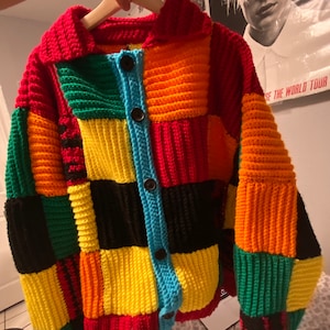 May include: A colorful crocheted cardigan with a patchwork design. The cardigan has a button closure and long sleeves. The colors include red, orange, yellow, green, black, and blue.
