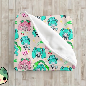 Może przedstawiać: Biały koc z polaru z kolorowym nadrukiem postaci z anime. Nadruk przedstawia zielone i różowe postacie z długimi włosami i dużymi oczami. Postacie otoczone są zielonymi liśćmi i różowymi kwiatami. Koc ma białą podszewkę z polaru.