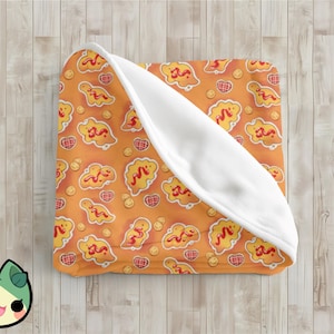 May include: A folded orange blanket with a repeating pattern of yellow fried food shapes with red sauce, smiley faces, and heart-shaped waffle designs. The blanket has a white, fluffy underside.