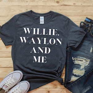Puede incluir: Una camiseta gris oscuro con el texto "Willie. Waylon And Me" impreso en blanco.