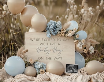 Può includere: Un cartello di legno con il testo "We're excited to say we have a Baby Boy on the way!" circondato da palloncini beige, fiori blu e bianchi e una piccola immagine di ecografia.