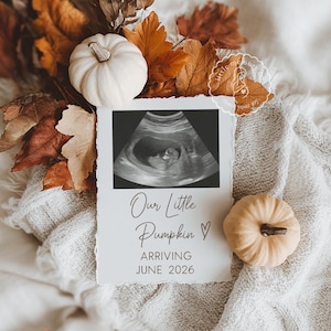 May include: A pregnancy announcement card with an ultrasound scan, pumpkins, and autumn leaves. The card says "Our Little Pumpkin" and "Arriving June 2026". The pumpkins are white and tan, and the leaves are brown and orange.