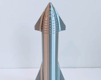 May include: A silver model rocket with a pointed nose cone and fin-like structures. The rocket is mounted on a black circular base. The design features detailed surface textures and a streamlined shape, suggesting a futuristic theme.
