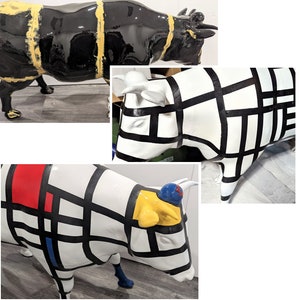 Op de afbeelding: Een verzameling decoratieve koeiensculpturen. E&eacute;n is zwart met gele strepen, een andere is wit met zwarte rasterlijnen en een derde heeft rode, blauwe en gele geometrische vormen. De sculpturen staan op een grijze ondergrond.