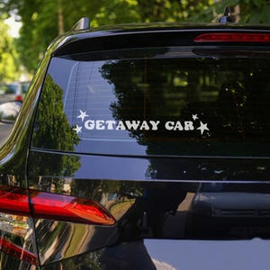 May include: A black car with a white sticker on the back window that says "GETAWAY CAR" with stars on either side of the text.