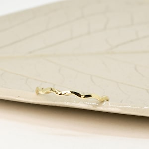 May include: A thin gold band ring with a wavy, textured design.