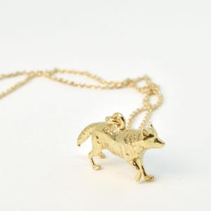 Può includere: Una collana con catena d'oro con un ciondolo a forma di lupo dorato dettagliato. Il lupo è in piedi su tutte e quattro le zampe e guarda a destra.